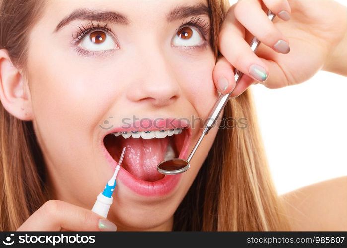 Dental health care, stomatology concept. Woman with braces having dentist appointment, looking at teeth with small mirror and cleaning using tiny toothbrush.. Woman with braces having dentist appointment