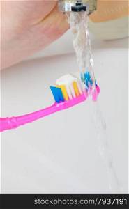 Dental health care. Toothpaste on toothbrush in woman hand, white bathroom sink and running faucet in background