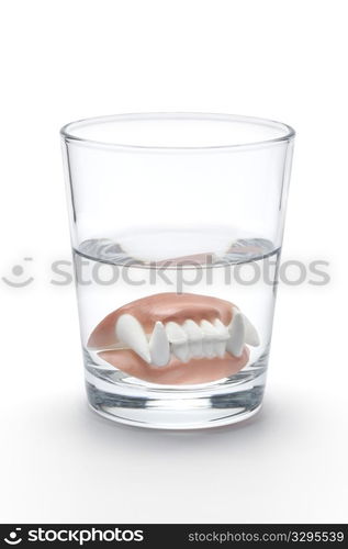 Dental prothesis of a vampire in a glass of water on white background