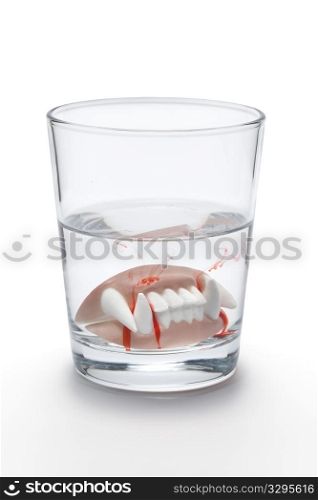 Dental prothesis with blood of a vampire in a glass of water on white background