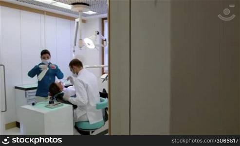 Dentist and assistant checking dental hygiene of female client. Sequence of steadicam wide and medium shots
