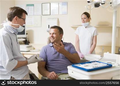Dentist and assistant in exam room with man in chair smiling