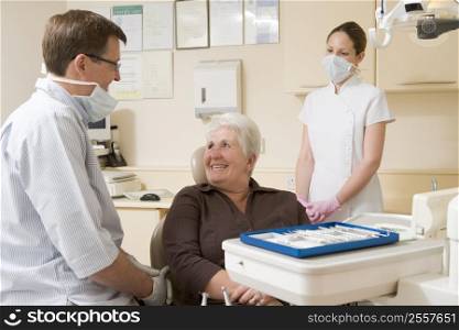 Dentist and assistant in exam room with woman in chair smiling