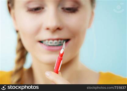 Dentist and orthodontist concept. Young woman with blue braces cleaning and brushing teeth using little toothbrush, interdental brush. Woman with teeth braces using interdental brush