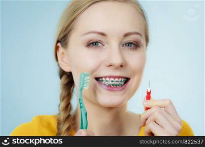 Dentist and orthodontist concept. Young woman with blue braces cleaning and brushing teeth using two different brushes, little interdental brush and manual toothbrush. Girl with teeth braces using interdental and traditional brush