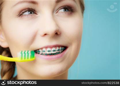 Dentist and orthodontist concept. Young woman with blue braces cleaning and brushing teeth using manual toothbrush, traditional brush. Woman with teeth braces using brush