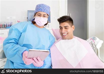 Dentist and patient commenting treatments in a tablet application in a consultation with medical equipment in the background. High quality photo.. Dentist and patient commenting treatments in a tablet application in a consultation with medical equipment in the background.