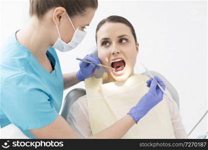 Dentist examining patient mouth with angled mirror and scaler at dental clinic