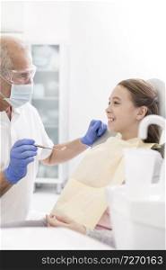 Dentist examining smiling girl patient at dental clinic