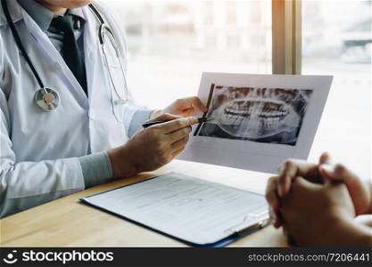 Dentist hand holding pen pointing x-ray picture and talking to the patient about medication and surgery treatment.