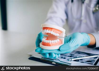 Dentist holding dentures in office room.