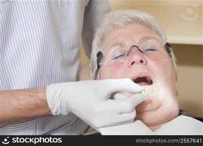 Dentist in exam room fitting dentures on woman in chair