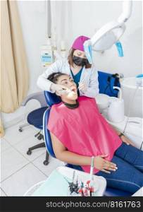 Dentist in his office examining female patient’s mouth. Female dentist examining mouth to teen girl lying on chair, Female dentist with probe and dental mirror examining young female mouth
