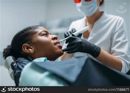 Dentist installs the seal on the tooth, woman in dental clinic. Female patient in dentistry cabinet, stomatology. Dentist installs the seal on tooth, dental clinic