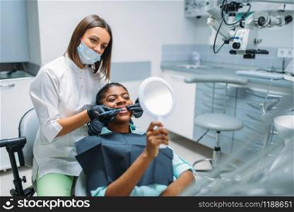 Dentist shows teeth to client. Female patient on whitening procedure in dental clinic. Woman in dentistry cabinet, stomatology