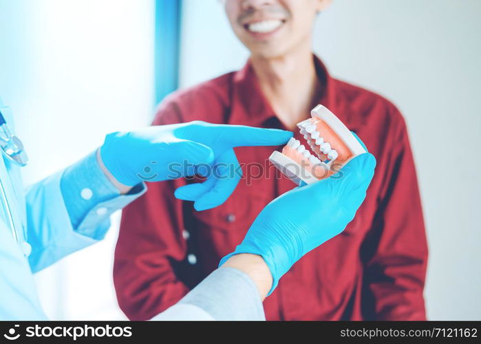 Dentist talking to smiling male patient and showing denture in dental office