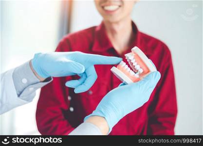 Dentist talking to smiling male patient and showing denture in dental office