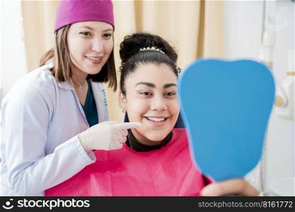 Dentist with satisfied patient smiling at dental mirror, Satisfied patient in dental clinic looking at mirror, female patient checking teeth after curing teeth in dental clinic.