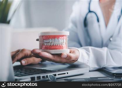 Dentist woman hand holding educational jaw model of oral cavity with teeth at workplace, female doctor sitting and hold tooth on desk at clinic office have laptop computer, dental concept