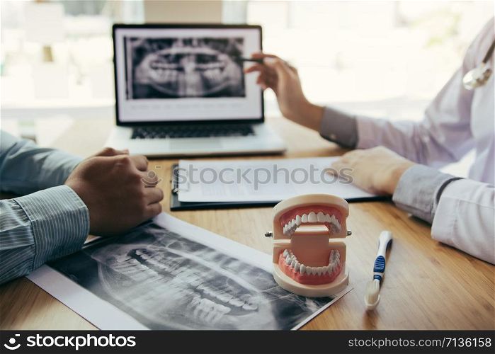 Dentists are discussing dental problems at report x-ray image on laptop screen to patients.