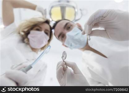 Dentists leaned over patient in dentist&rsquo;s chair at clinic. Doctors with mask and tools.