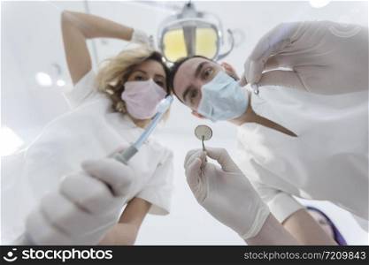 Dentists leaned over patient in dentist&rsquo;s chair at clinic. Doctors with mask and tools.