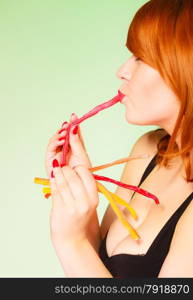 Dependence on sweets. Young red haired woman with candy on green background in studio.