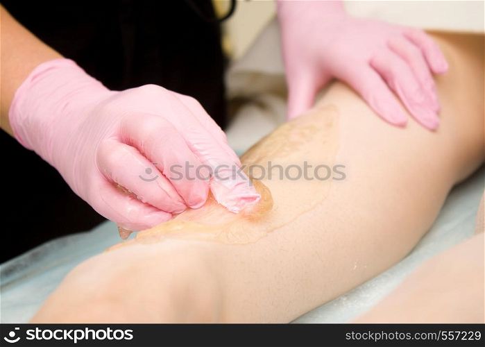 depilation and beauty concept - procedure of hair removing on leg beautiful woman with sugar paste or wax honey and pink gloves hand. procedure of hair removing on leg beautiful woman with sugar paste or wax honey and pink gloves hand - depilation and beauty concept