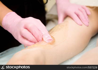 depilation and beauty concept - procedure of hair removing on leg beautiful woman with sugar paste or wax honey and pink gloves hand. procedure of hair removing on leg beautiful woman with sugar paste or wax honey and pink gloves hand - depilation and beauty concept