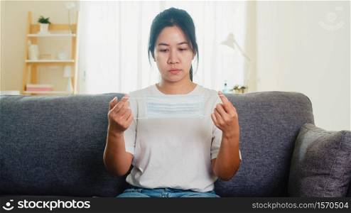 Depressed Asian business woman wearing protective mask sitting on sofa in living room at house when social distancing stay at home and self quarantine time, pandemic in china, coronavirus concept.