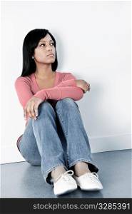 Depressed black woman sitting against wall on floor looking away