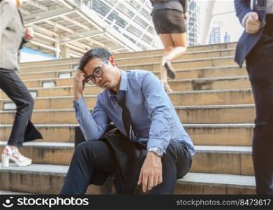 Depressed business man sitting still on busy stairs outdoors with blurry businesswomen walking past him in the city. Jobless man despair economic crisis, business failure or global economy recession