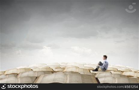 Depressed businessman in isolation. Young businessman sitting alone on pile of old books