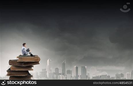 Depressed businessman in isolation. Young businessman sitting alone on pile of old books