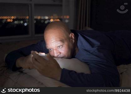 Depressed elderly black man. African American people using a smartphone on social media internet and sleeping on bed in bedroom at home. Lifestyle on late night in technology device concept. Insomnia.