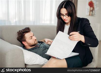Depressed man lies on sofa at psychotherapist reception. Female doctor writes notes in notepad, professional psychology support. Man lies on sofa at psychotherapist reception