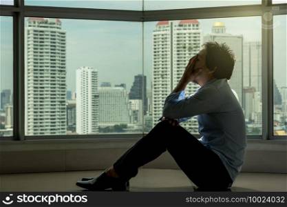 depressed man sitting head in hands on the interior Skyscraper with low light environment beside the windows over the cityscape background, dramatic concept