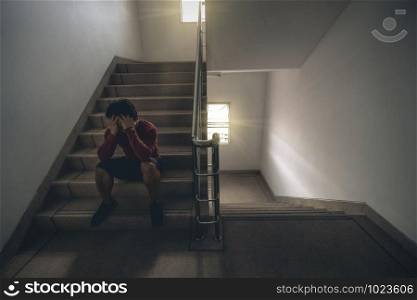 Depressed man sitting head in hands on the staircase in the fire escape or building stair with low light environment, dramatic scene concept