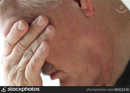 Depressed older man averts his head, covering his eyes with a hand.