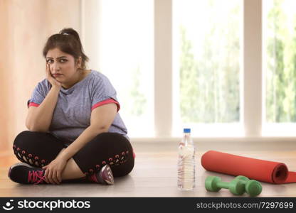 Depressed overweight woman sitting on the floor and doesn't wont to exercise