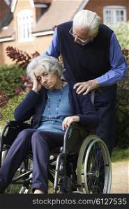 Depressed Senior Woman In Wheelchair Being Pushed By Husband