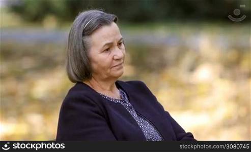 Depressed senior woman thinking worried outdoors in park.