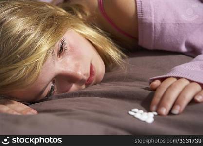 Depressed Teenage Girl Sitting In Bedroom With Pills
