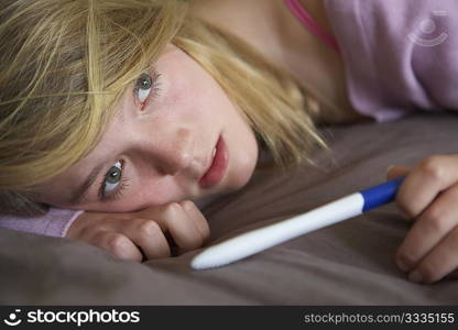 Depressed Teenage Girl Sitting In Bedroom With Pregnancy Test