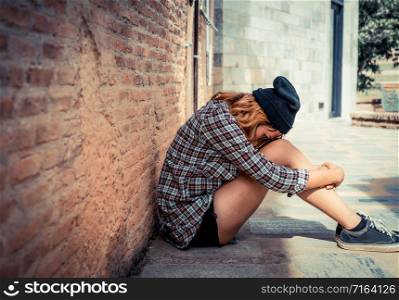 Depressed teenage woman feeling sad alone against brick wall in old town. Education and family failure concept.