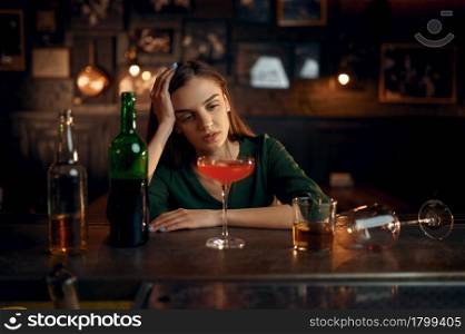 Depressed woman drinks different alcohol at the counter in bar. One female person in pub, human emotions, leisure activities, nightlife. Depressed woman drinks alcohol at counter in bar