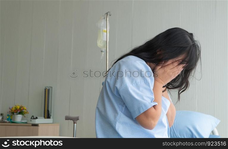 Depressed woman sitting alone on patient bed at hospital. She pain looking negative and worried for her bad health and suffering depression. Concept of healthcare patient lifestyle and medical.