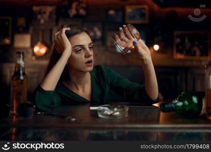 Depressed woman sitting at the counter in bar, full ashtray. One female person in pub, human emotions, leisure activities, depression. Depressed woman sitting in bar, full ashtray