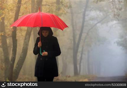 Depressed woman with red umbrella and foggy forest