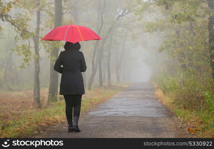 Depressed woman with red umbrella and foggy forest
